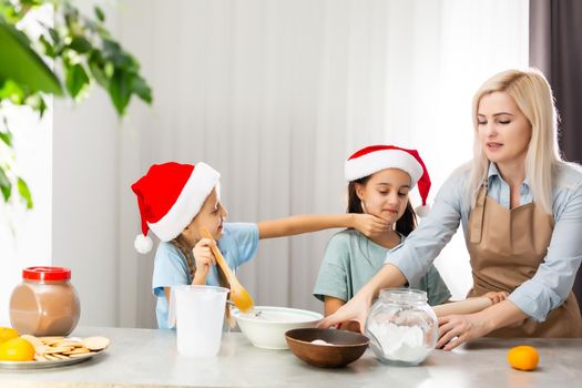 Happy family in the kitchen. Mother and two little daughters preparing the dough for Christmas cookies.