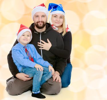 Happy family of 3 people in caps of Santa Claus, the Christmas tree and the fireplace in the Christmas night.Brown festive, Christmas background with white snowflakes, circles.