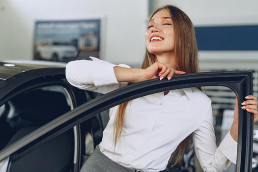 Beautiful young woman touching her new car with pleasure and joy