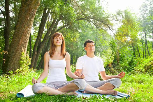 Young man and woman doing yoga. Lotus pose meditation in a garden. Outdoor full body