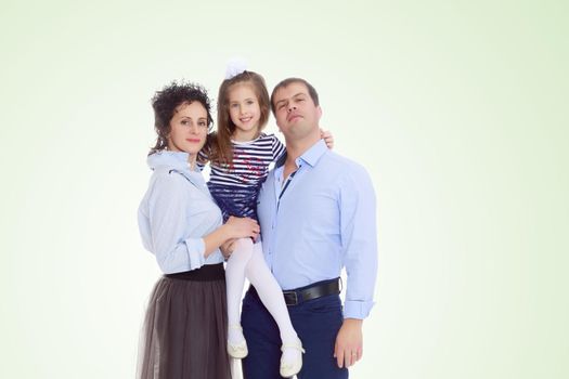 Happy young family, mom dad and little daughter.Parents keep the girl in her arms , and she hugs their neck.On a yellow gradient background.