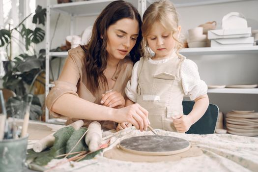 Woman and girl kneading clay. Family make art product at table in pottery workshop. Mother with daughter.