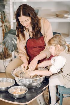 Woman and girl kneading clay. Family make art product at table in pottery workshop. Mother with daughter.