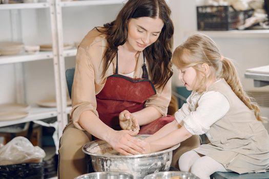 Woman and girl kneading clay. Family make art product at table in pottery workshop. Mother with daughter.