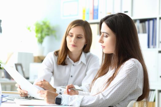 Portrait of joyful businesswoman sitting indoors with friendly colleague and looking at important project in paper folder with charts and graphs. Accounting office concept