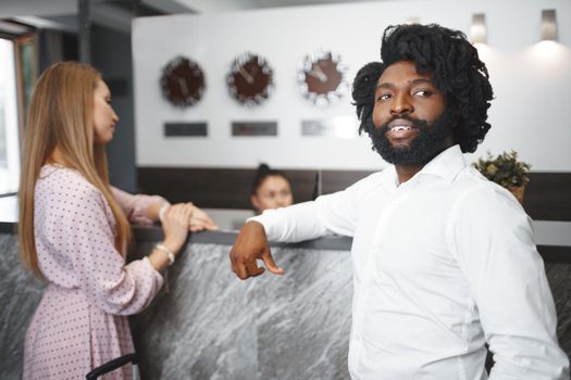 Business trip concept. Black man and caucasian woman businesspeople colleagues checking-in in hotel reception desk