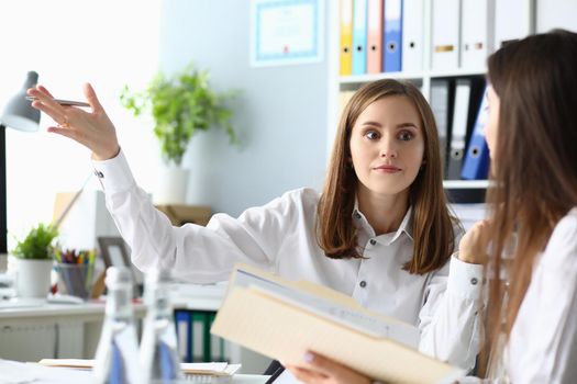 Portrait of pretty businesswoman sitting indoors and talking about important profitable project with friendly female manager. Accounting workplace concept