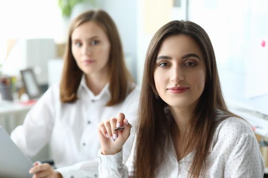 Portrait of joyful businesswoman sitting in modern workplace and looking at camera with calmness. Pretty woman discussing important important profitable strategy. Accounting workplace concept