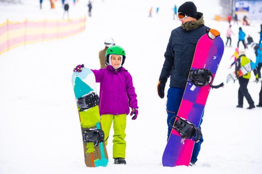 Instructors teach a child on a snow slope to snowboard