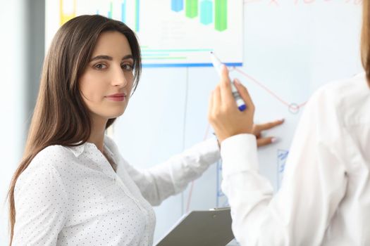 Portrait of smart businesswoman sitting in modern workplace and pointing at something on modern glass board with tender hand. Accounting office concept