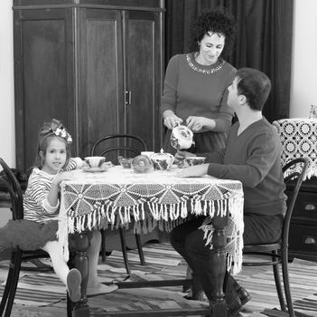 A family of three in the interior of the fifties of the last century, drinking tea for lace tablecloth vintage oak table.Black-and-white photo. Retro style.