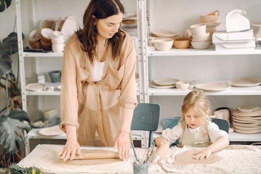 Woman and girl kneading clay. Family make art product at table in pottery workshop. Mother with daughter.