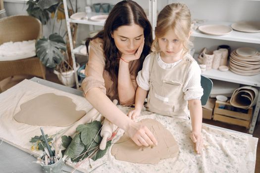 Woman and girl kneading clay. Family make art product at table in pottery workshop. Mother with daughter.