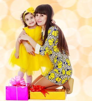 Beautiful young mother and her cute little daughter , embracing, surrounded by Christmas gifts.Winter brown abstract background with white snowflakes.