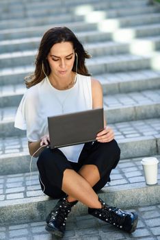 Middle-age businesswoman working with her laptop computer sitting on urban steps outdoors.