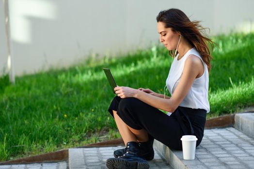 Young businesswoman having a videoconference with her laptop computer sitting on urban steps outdoors.