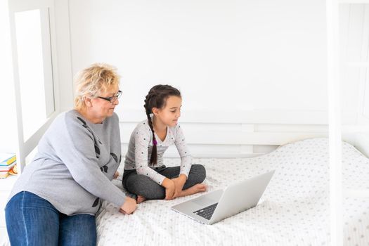 Cute and happy little girl child using laptop computer with her grandma, studying through online e-learning system.