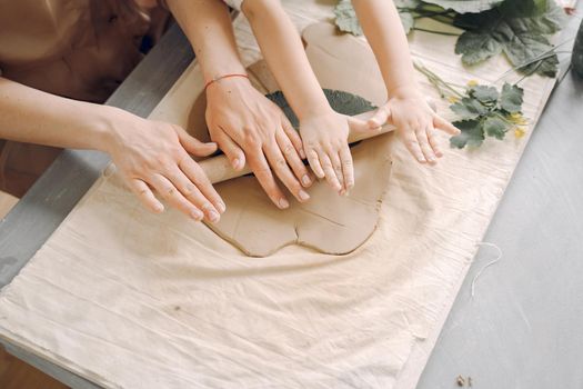 Woman and girl kneading clay. Family make art product at table in pottery workshop. Mother with daughter.