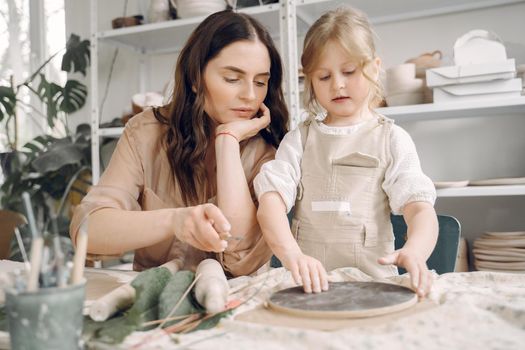 Woman and girl kneading clay. Family make art product at table in pottery workshop. Mother with daughter.