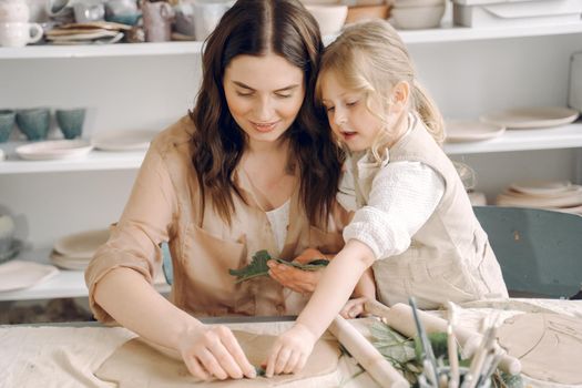 Woman and girl kneading clay. Family make art product at table in pottery workshop. Mother with daughter.