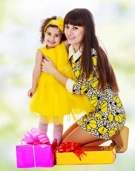 Beautiful young mother and her cute little daughter , embracing, surrounded by Christmas gifts.white-green blurred abstract background with snowflakes.