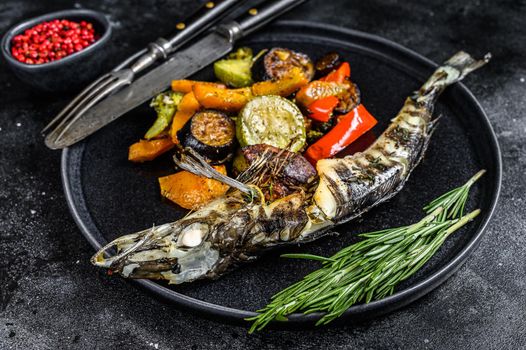 Baked whole icefish with grilled vegetables. Black background. Top view.