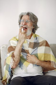 Senior man alone sitting on sofa. Sick man covered with plaid. Grangfather with cup of tea.