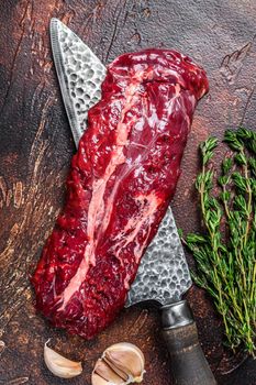 Raw organic machete or skirt steak on a butcher knife . Dark background. Top view.