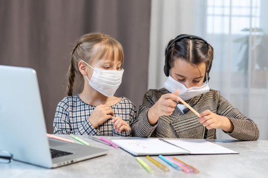 Young elementary school girls with face protective mask watching online education class. Coronavirus or Covid-19 lockdown education concept.