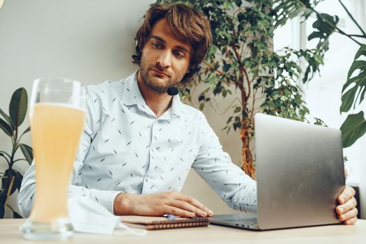 Bearded man using his laptop while drinking glass of beer sitting at his table