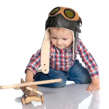 The boy in the helmet of the pilot plays with a toy wooden plane. He dreams of becoming a pilot. Concept of happy childhood, child in the family.Isolated on white background.