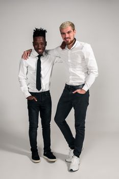 Joyful relaxed african and caucasian boys in white and black office clothes laughing and posing at white studio background with copy space. Full-length photo