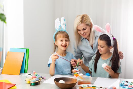 Young mother and her two daughters painting Easter eggs