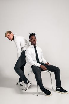 Two stylish men posing and having fun on white background. Friends. Two guys in white shirts and dark pants at studio