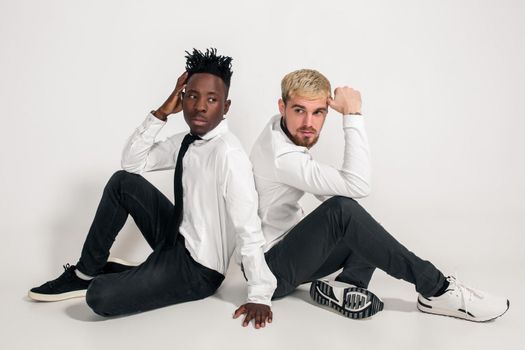 Friends. Two guys in white shirts and dark pants posing in the studio on a white background. Copy space. Two friends are sitting on the floor