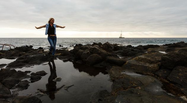 Women on volcanic rocks and blue ocean with waves, white foam and volcanic rocks. Canary Islands. The magnificent coast of the Atlantic Ocean.