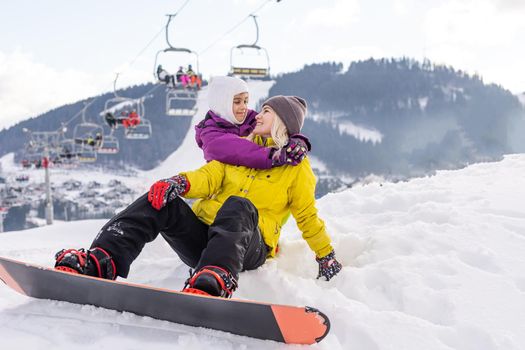 Mother and daughter with snowboards are playing in the snow