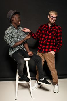 A Friend portraits shot against dark background. Two best friends are posing and having fun in the studio. Dressed in casual clothes, shirts in a cage.