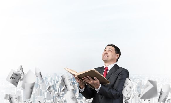 Happy businessman looking up with open book. Smiling man in suit standing on downtown background with falling paper documents. Lawyer holding legal regulation book. Business accounting and consulting