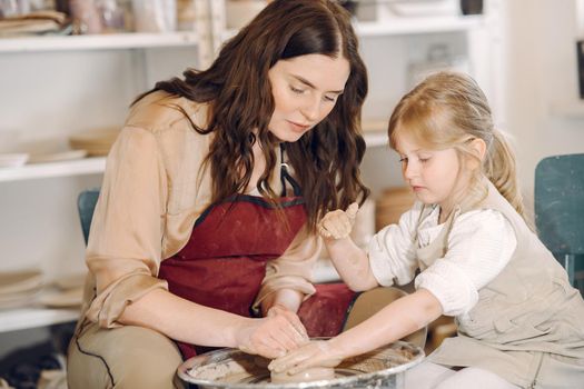 Woman and girl kneading clay. Family make art product at table in pottery workshop. Mother with daughter.