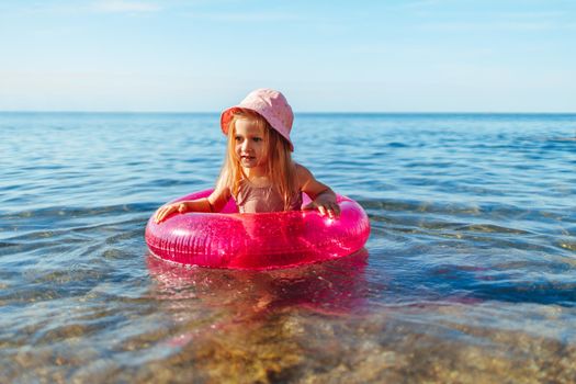 Happy little girl bathing in sea with pink circle and hat