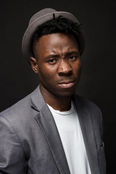 Portrait of a fashionable african american man smiling on black background. A nice guy in a gray jacket and a white T-shirt on a dark studio background. A large portrait