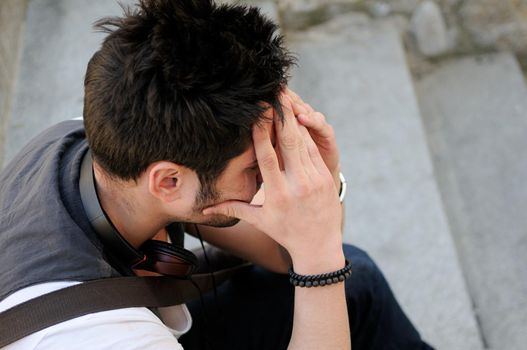 Portrait of young pensive man sitting on steps, with headphones