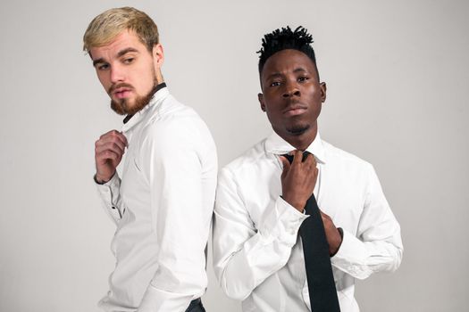 International friendship concept. Studio shot of two stylish young men: handsome bearded young man in white shirt and jeans standing next to his African-American friend on white background