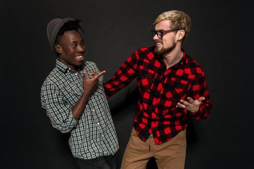 A Friend portraits shot against dark background. Two best friends are posing and having fun in the studio. Dressed in casual clothes, shirts in a cage.