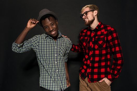 A Friend portraits shot against dark background. Two best friends are posing and having fun in the studio. Dressed in casual clothes, shirts in a cage.