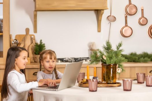 Two little girls watching online school while sitting at table dining room table.