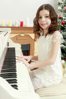 Adorable little girl new year's eve on the backdrop of the Christmas tree plays the piano.