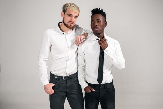 Joyful relaxed african and caucasian boys in white and black office clothes laughing and posing at white studio background with copy space. Belt portrait