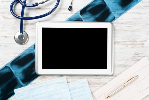 Laboratory result of patient examination lies on doctor table. Top view tablet computer with blank screen, x-ray image, stethoscope and cardiogram on wooden desk. Digital technology in cardiology.
